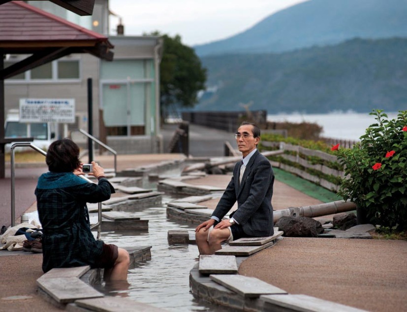 Turistas en un ashiyu, unas aguas termales para los pies, junto al volcán de Sakurajima. Tarumisu, Kagoshima, 2010. 桜島をバックに足湯を楽しむ観光客。鹿児島県垂水市、2010年。 COPYRIGHT:Tina Bagué