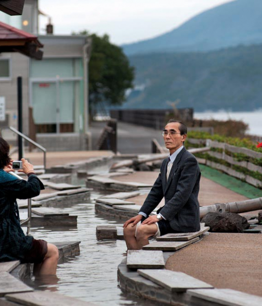 Tourists in an ashiyu, a hot spring for the feet, in front of Sakurajima volcano. Tarumisu, Kagoshima, 2010. 桜島をバックに足湯を楽しむ観光客。鹿児島県垂水市、2010年。 COPYRIGHT:Tina Bagué Tourists in an ashiyu, a hot spring for the feet, in front of Sakurajima volcano. Tarumisu, Kagoshima, 2010. 桜島をバックに足湯を楽しむ観光客。鹿児島県垂水市、2010年。 COPYRIGHT:Tina Bagué