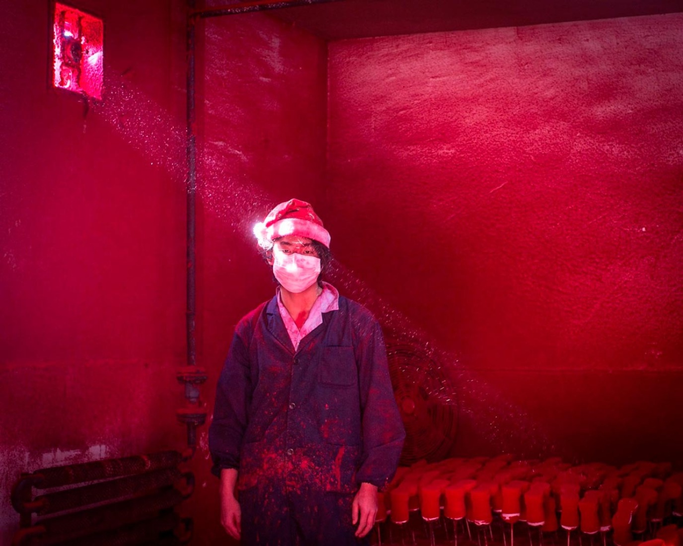 Christmas Factory Ronghui Chen. Contemporary Issues 2015. Segundo premio individuales. Wei, un trabajador chino de 19 años de edad, llevaba una mascarilla y un gorro de Papá Noel, se encuentra junto a las decoraciones de Navidad que se están secando en una fábrica en forma de polvo rojo que se utiliza como colorante se cierne en el aire.