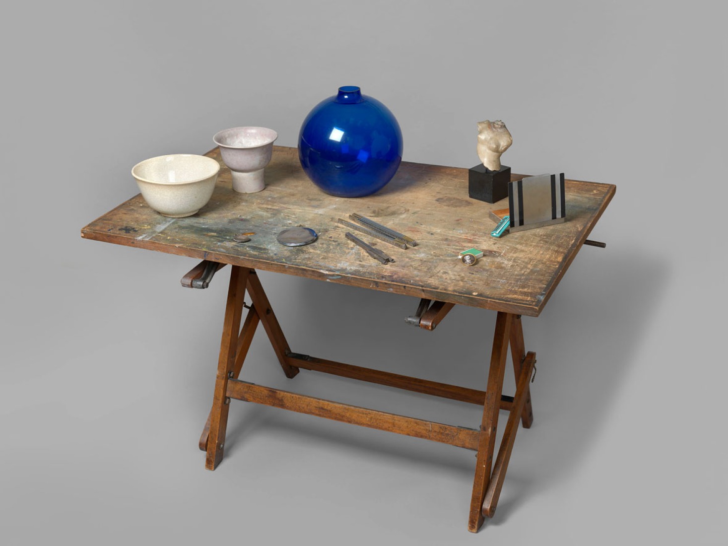 Table with blue glass vase, beach pebble on stand, African sculpture on lacquered base, Greek torso on marble base, two ceramic bowls and one small wooden easel. Exhibition Eileen Gray: the private painter. Image courtesy of the Osborne Samuel Gallery.  Table with blue glass vase, beach pebble on stand, African sculpture on lacquered base, Greek torso on marble base, two ceramic bowls and one small wooden easel. Exhibition Eileen Gray: the private painter. Image courtesy of the Osborne Samuel Gallery.
